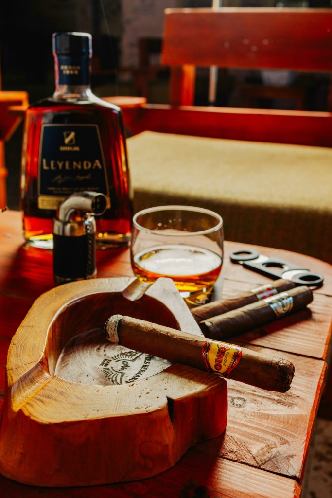 a wooden table topped with a bottle of liquor and a cigar